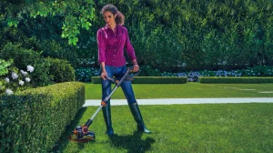 Woman using a string trimmer to edge neatly around garden hedges