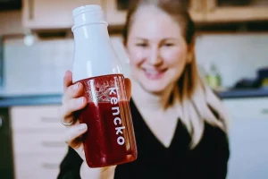 Smiling woman holding a red Kencko Smoothie in a shaker bottle.
