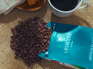 Lifeboost Coffee beans spilled with cup of brewed coffee