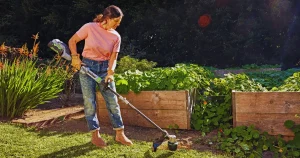 Woman using a string trimmer to edge around raised garden beds
