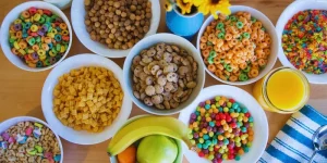 Assorted colorful bowls of All Cereals with fruit and juice.